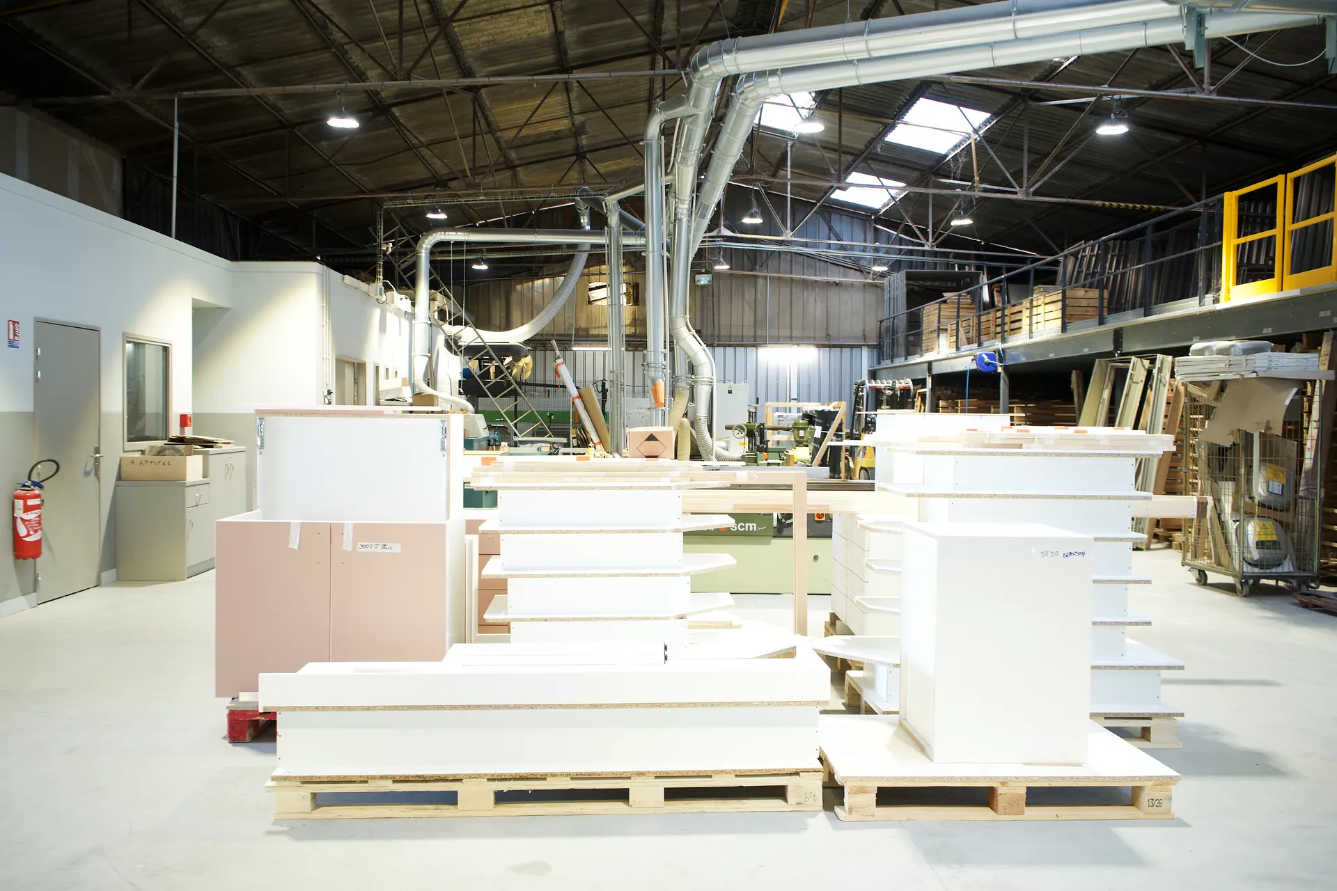 Caissons de mobilier sur mesure blancs et rose poudré en cours de fabrication, sur palettes, dans l'atelier BMA BY LEGRAND