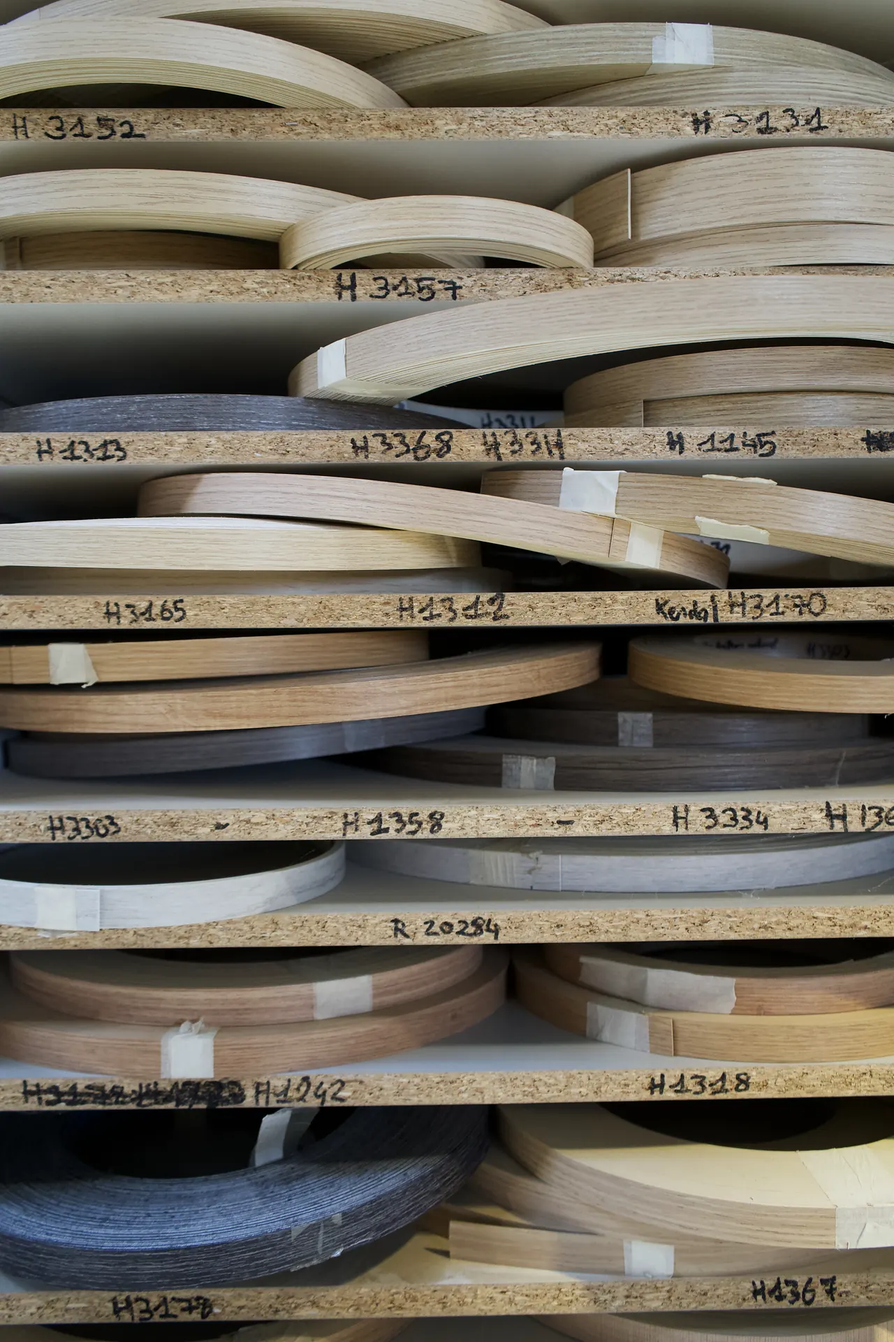 Rouleaux de bandes de chant aux décors bois, gris et blanc, rangés sur des étagères repérées par référence